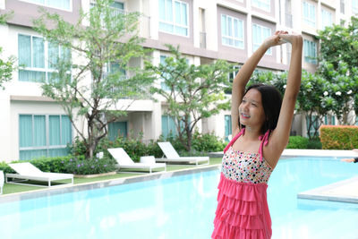 Cute girl with arms raised standing by building