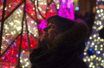 Happy beautiful woman wearing fur clothing against illuminated decoration