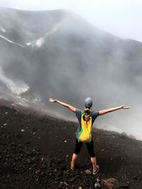 Rear view of woman standing with arms outstretched at volcanic crater