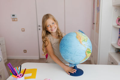 Elementary school student is sitting at a table with a globe on it and smiling