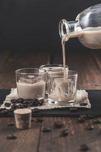 Pouring cream coffee liqueur in glasses with ice on dark wooden background. vertical format.