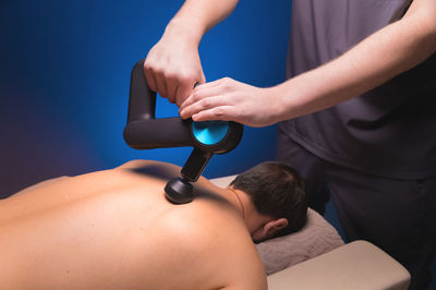 Therapist massaging a man's back with a percussion massage device in a massage room. the therapist's