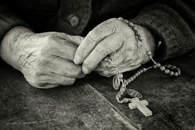 Close-up of hands holding rosary at table