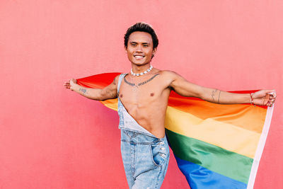 Man with rainbow flag against pink wall