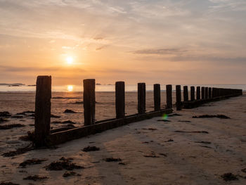 Wooden posts on beach against sky during sunset