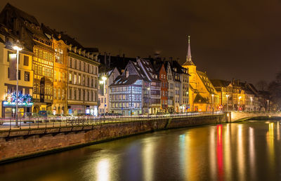 Illuminated buildings by river against sky in city at night