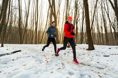 Man and woman running together through woods in winter.