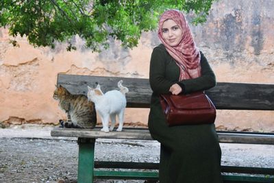 Portrait of woman in hijab sitting with cats on bench