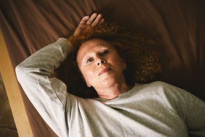 High angle view of thoughtful senior woman lying on bed at home