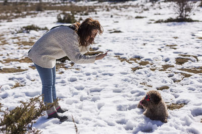 Woman photographing dog on snow covered land