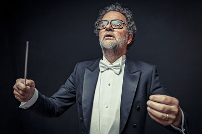 Midsection of man holding eyeglasses against black background