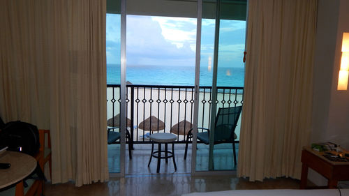 Chairs and table by sea against sky seen through window