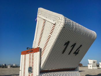 Traditional north german white beach chair with black number 114 at north sea beach against blue sky