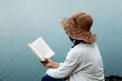 Rear view of woman holding book against water