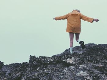 Rear view of woman walking on rock against clear sky