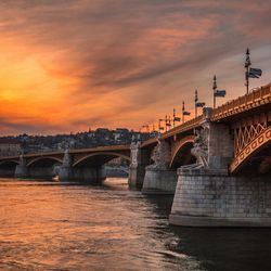 Bridge over river in city against sky at sunset