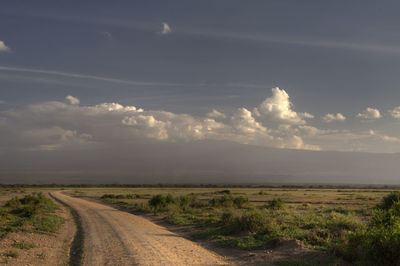 Dirt road passing through landscape against sky