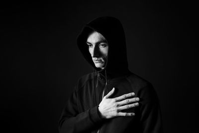 Portrait of young man standing against black background