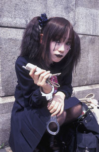 Young woman wearing make-up with handcuffs holding phone while sitting on steps