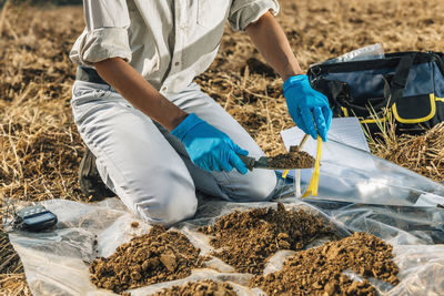 Low section of agronomist analyzing soil on field