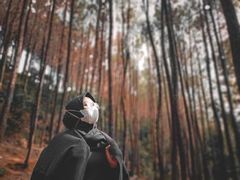 Portrait of man standing by tree trunk in forest