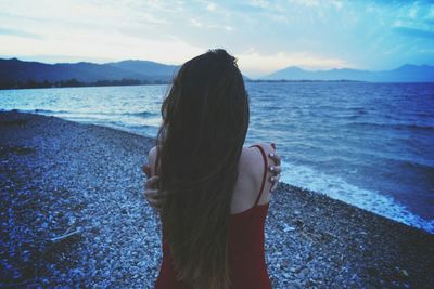 Rear view of woman giving herself hug on beach at dusk