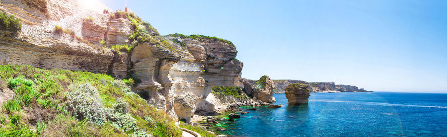 Scenic view of cliff by sea against clear blue sky