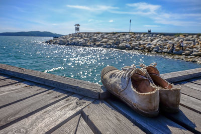 Low angle view of shoes on pier at sea against sky