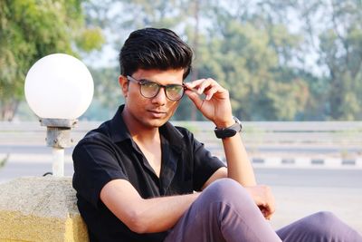 Young man wearing eyeglasses sitting by road