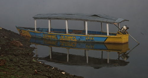 Fishing boat moored in lake against sky