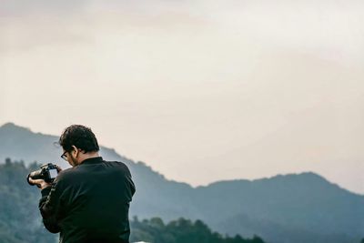 Side view of man photographing against sky