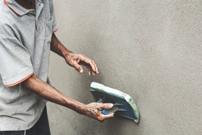Asian male worker plasterer using a plastering sponge float on an outdoor cement wall 