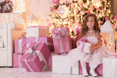 A beatiful girl with curly hair in white dress is holding of christmas box gift and sitting