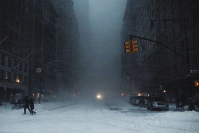 Snow covered city street by buildings in city