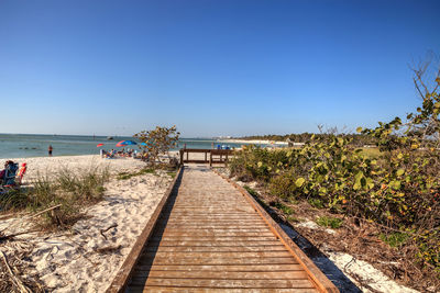 Footpath leading towards sea against clear blue sky