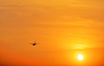 Silhouette airplane flying against orange sky