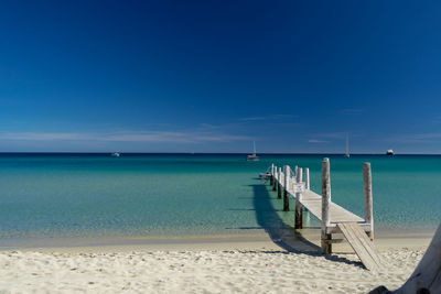 Wooden posts in sea against blue sky