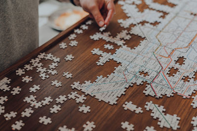 Jigsaw puzzle on a table, male hand with a piece of the background, selective focus.