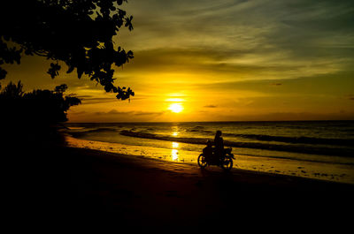 Silhouette people riding on beach against sky during sunset