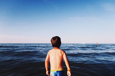 Rear view of shirtless man standing in sea against clear sky