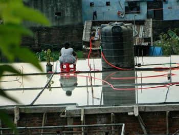 Rear view of woman sitting by storage tank at building terrace