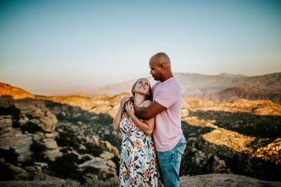 Biracial couple hugging and looking at each other on a mountain top