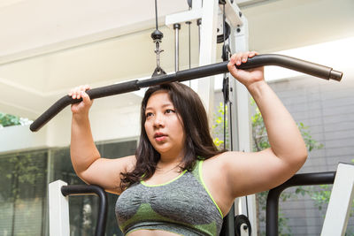 Overweight young woman looking away while exercising in gym