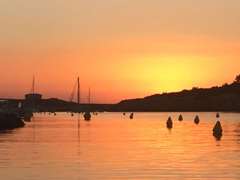 Silhouette sailboats in sea against orange sky