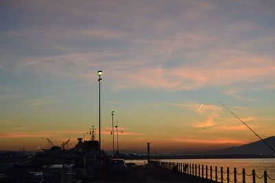 Silhouette street by sea against sky during sunset