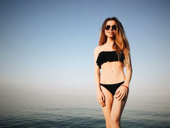 Portrait of young woman standing at beach against sky