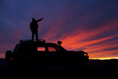 Silhouette man standing car against orange sky