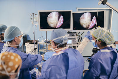 Doctors monitoring surgery on computer screen while standing at operating room during covid-19