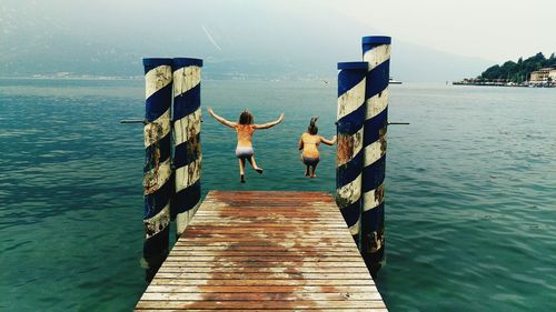 Rear view of young women jumping from pier over sea