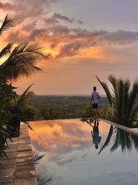 Rear view of man standing by swimming pool against sky during sunset